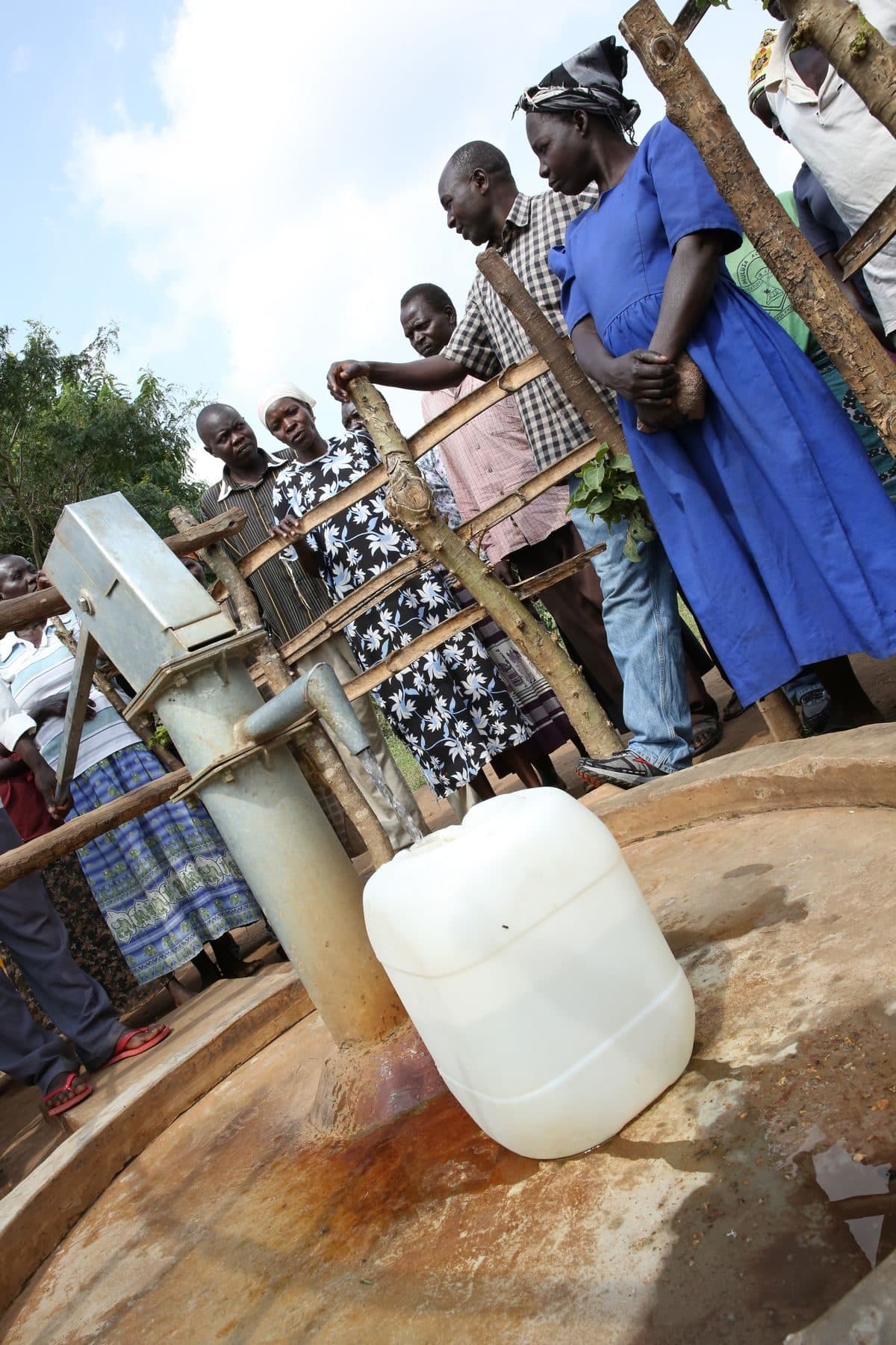 Women and children filling jerrycans at a hand pump on a newly completed water well