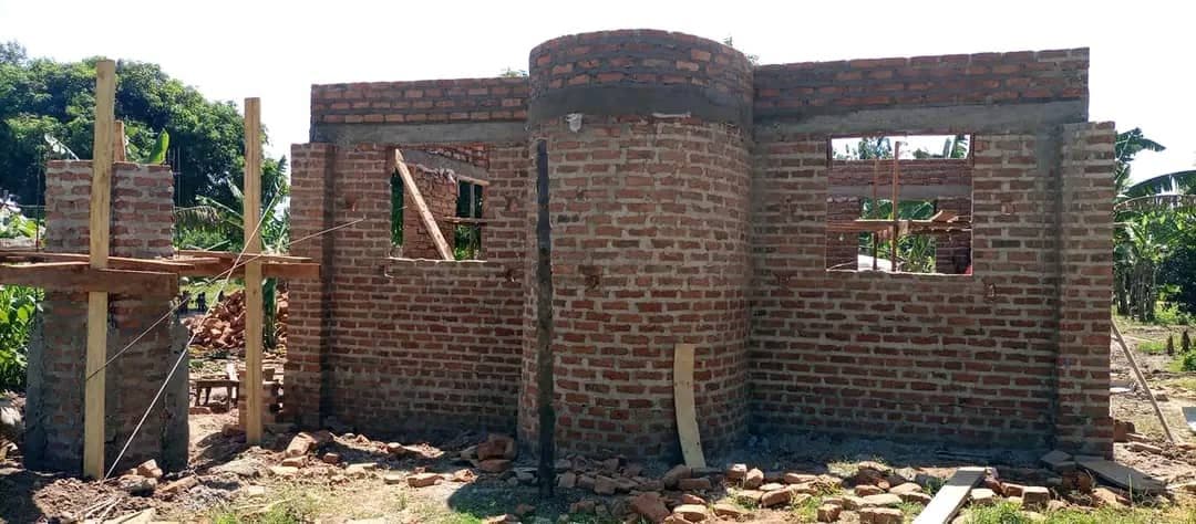 Builders working on the brick walls of a mosque under construction, with timber roof trusses going up