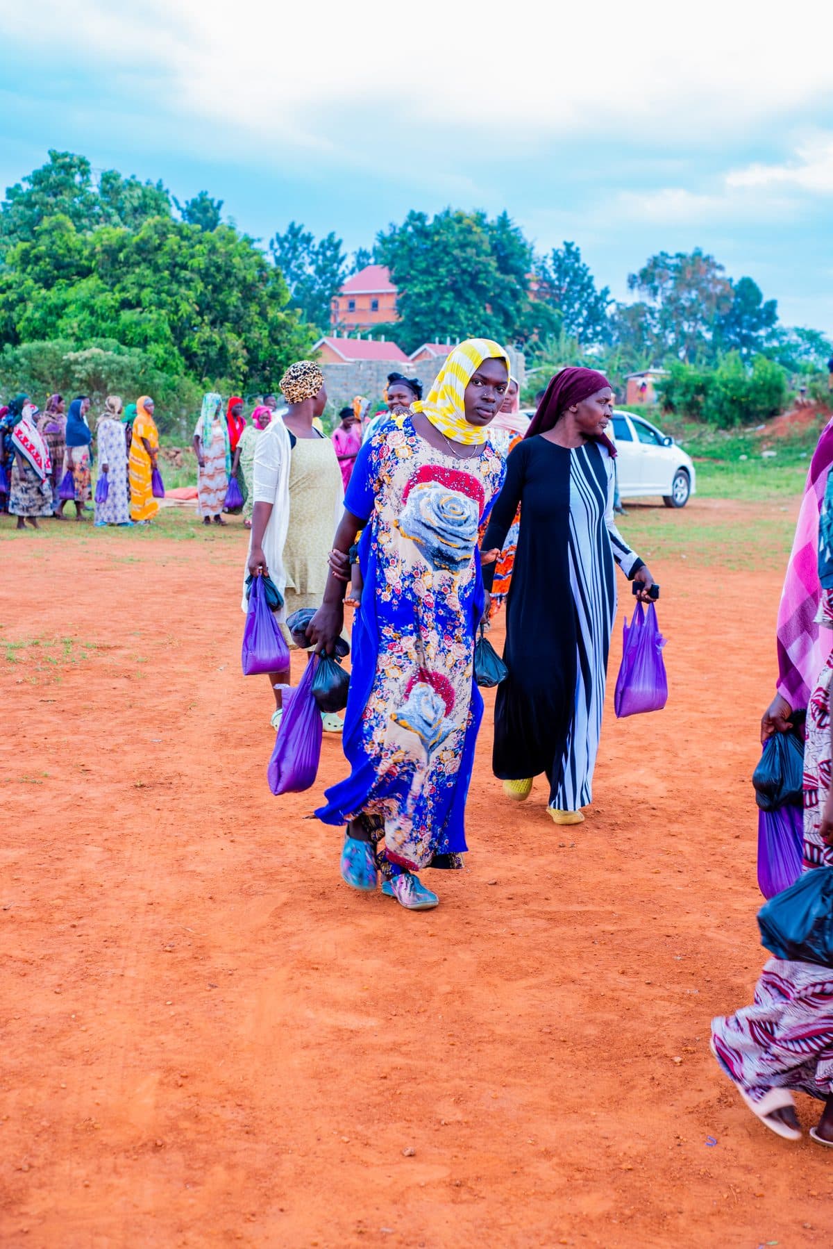 Women in brightly patterned dress walking home carrying the food parcels they have just received