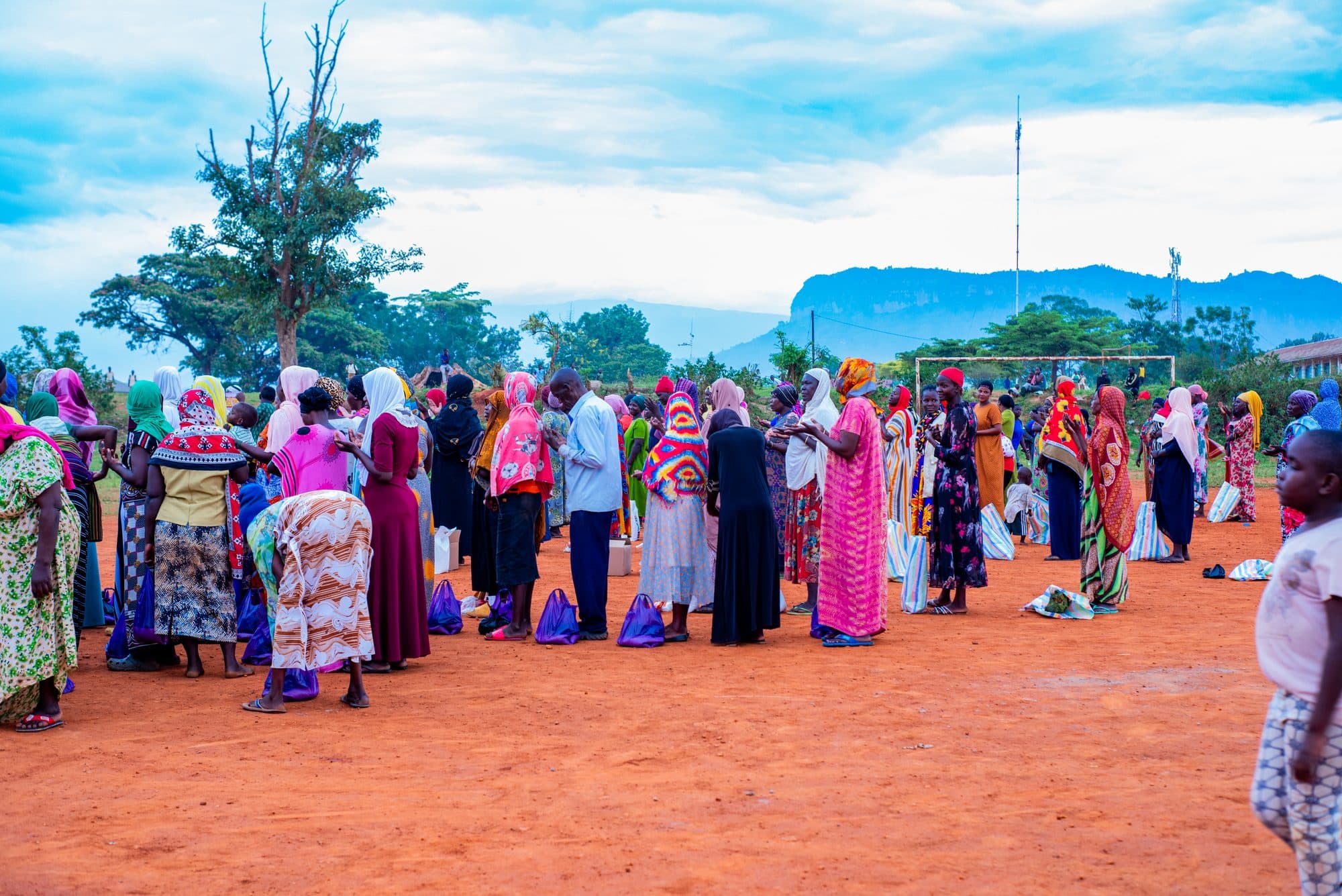 Dozens of women and men gathered on the red earth of a village field at an HCIU food distribution, carrying away their parcels beneath a wide sky and distant hills