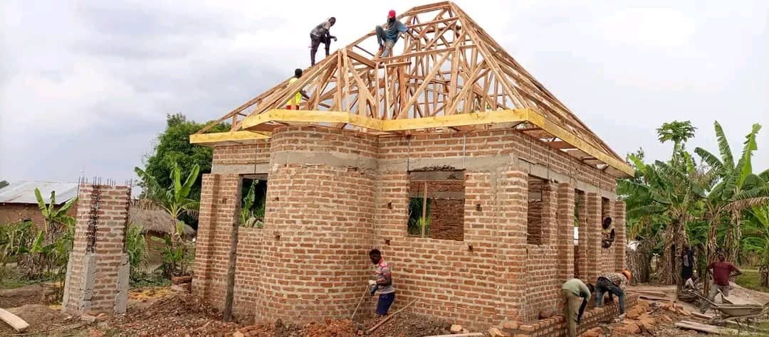 Builders raising timber roof trusses onto the brick walls of a mosque under construction